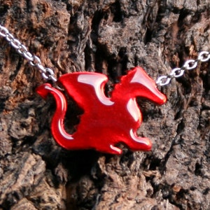 Può includere: Una collana con catena d'argento con un ciondolo a forma di drago rosso. Il drago è in una posa di volo con le ali spiegate.