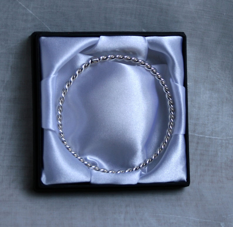 May include: A silver twisted bangle bracelet in a white satin lined box.
