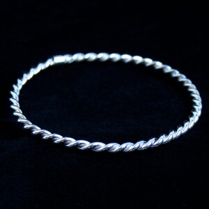 May include: A silver twisted bangle bracelet. The bracelet is made of a single piece of metal that is twisted into a rope-like design.