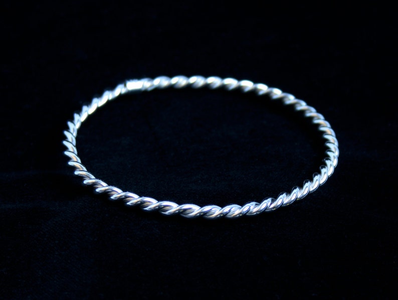 May include: A silver twisted bangle bracelet. The bracelet is made of a single piece of metal that is twisted into a rope-like design.