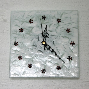 May include: A white square clock with black hands and a gold center. The clock face is decorated with red flower accents.