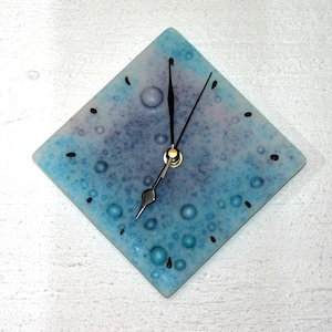 May include: A square clock with a blue and purple background with white and blue bubbles. The clock has black hands and a gold center.
