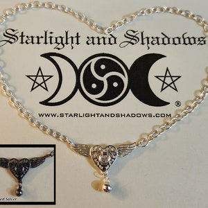 May include: Silver necklace with a heart pendant featuring wings and a bell charm. The pendant has a delicate filigree design. The necklace is on a white background with the text "Starlight and Shadows" and a website address.