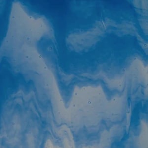 Op de afbeelding: Abstract blauw en wit glas met een vloeiend, gemarmerd uiterlijk. Het ontwerp heeft wervelende patronen van lichtblauw en wit, waardoor een dynamisch en gestructureerd visueel effect ontstaat. Het glas heeft een doorschijnende kwaliteit.