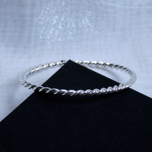 May include: A silver bangle bracelet with a twisted rope design.