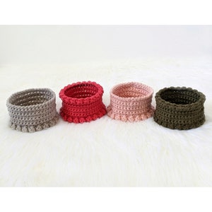 Puede incluir: Cuatro cestas de crochet en diferentes colores: gris, rojo, rosa y verde. Las cestas tienen un borde rizado y est&aacute;n hechas con un hilo texturizado.