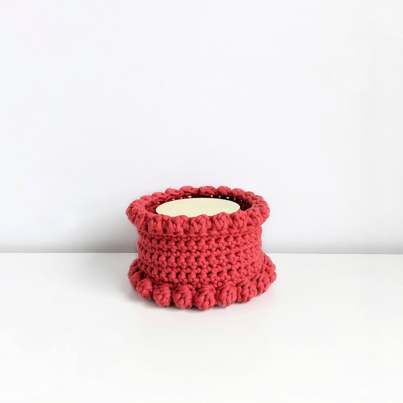 Puede incluir: Un portavelas de crochet rosa con un interior blanco y un borde rizado.
