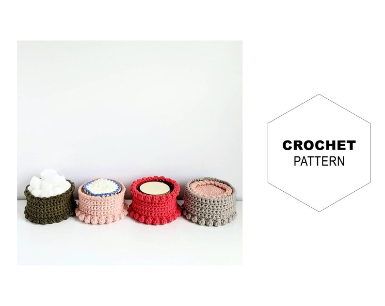 Puede incluir: Cuatro cestas redondas de ganchillo en diferentes colores: verde oliva, rosa, rojo y gris. Las cestas est&aacute;n alineadas en una fila sobre una superficie blanca.  CROCHET PATTERN est&aacute; escrito en una forma hexagonal en el fondo.