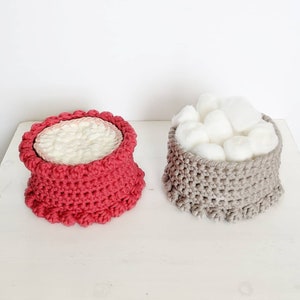 Puede incluir: Dos cestas de crochet, una roja y otra gris, con un relleno de bolas de algod&oacute;n blancas en la cesta gris.
