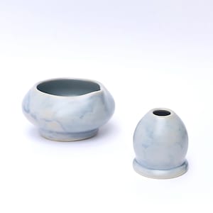 May include: Two light blue ceramic pieces. One is a small, rounded bowl with an irregular rim. The other is a small, egg-shaped vase with a narrow opening at the top. Both have a marbled appearance.