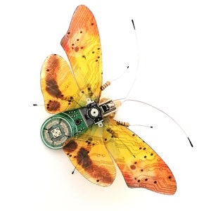 Puede incluir: Una mariposa amarilla y naranja con un diseño de placa de circuito en sus alas. La mariposa tiene una pequeña placa de circuito verde unida a su cuerpo.