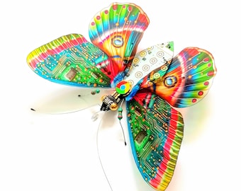 May include: A colorful butterfly made from circuit boards and other recycled materials. The butterfly has a green, blue, red, and yellow pattern. The wings are decorated with a circuit board design.