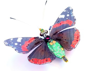 May include: A butterfly with black, red, and white wings has a circuit board for a body. The circuit board is green with gold-colored connectors.