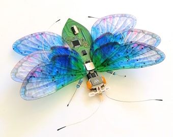 May include: A blue and green butterfly with translucent wings made from circuit boards and other electronic components. The butterfly is mounted on a white background.