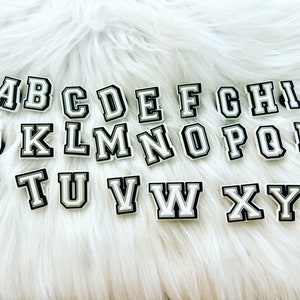 May include: White plastic letters of the alphabet with black outlines, arranged in alphabetical order on a white fuzzy surface.