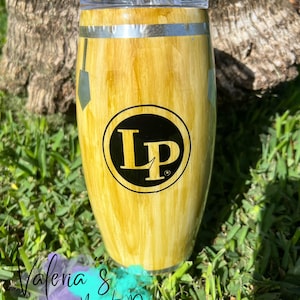 May include: A stainless steel tumbler with a woodgrain design and a black and gold LP logo. The tumbler is sitting on a bed of green grass.