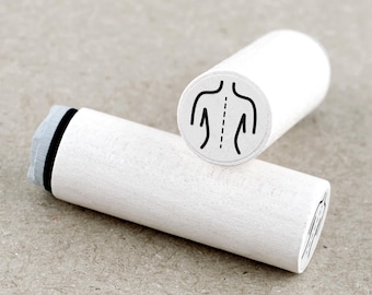 May include: Two white wooden stamps with a black outline of a human back. One stamp is angled, showing the back design, while the other is lying down. The stamps are on a neutral-toned surface.