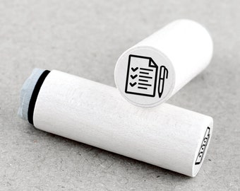 May include: White wooden stamp with a black line drawing of a checklist and pen. The stamp is cylindrical and has a rounded top.