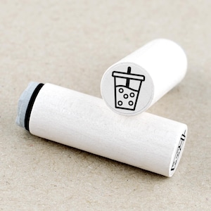 Op de afbeelding: Twee witte houten stempels met een zwart-wit bubble tea ontwerp. Eén stempel toont het ontwerp, terwijl de andere schuin staat, waardoor de houten handgreep en de rand van de stempel zichtbaar zijn. Deze stempels zijn voor knutselen en briefpapier.