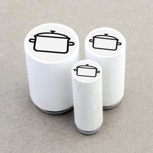 DE: Drei runde Ministempel mit dem Motiv 'Kochtopf' im direkten Größenvergleich: Ø 1,1 cm, Ø 1,5 cm und Ø 2 cm. Die kleinen Motivstempel bestehen aus weiß lackiertem Ahornholz mit schwarzer Zwischenlage und transparentem Motivaufkleber.
EN: Three round mini rubber stamps with the 'Cooking Pot' design in a direct size comparison: Ø 1.1 cm, Ø 1.5 cm and Ø 2 cm. These small rubber stamps are made of white lacquered maple wood with a black cushioning layer and a transparent label.