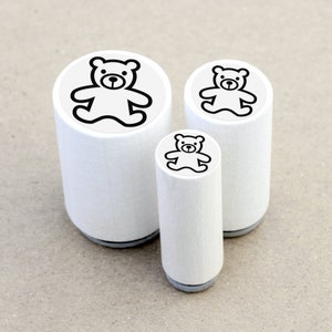 DE: Drei runde Ministempel mit dem Motiv 'Teddybär' im direkten Größenvergleich: Ø 1,1 cm, Ø 1,5 cm und Ø 2 cm. Die kleinen Motivstempel bestehen aus weiß lackiertem Ahornholz mit schwarzer Zwischenlage und transparentem Motivaufkleber.
EN: Three round mini rubber stamps with the 'Teddy Bear' design in a direct size comparison: Ø 1.1 cm, Ø 1.5 cm and Ø 2 cm. These small rubber stamps are made of white lacquered maple wood with a black cushioning layer and a transparent label.