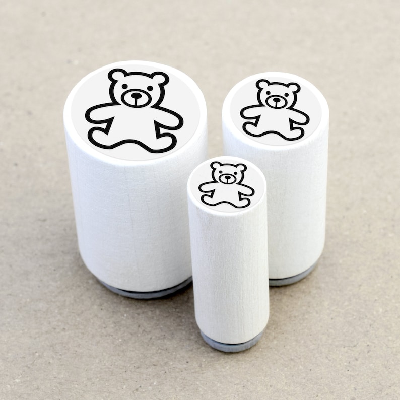 DE: Drei runde Ministempel mit dem Motiv 'Teddybär' im direkten Größenvergleich: Ø 1,1 cm, Ø 1,5 cm und Ø 2 cm. Die kleinen Motivstempel bestehen aus weiß lackiertem Ahornholz mit schwarzer Zwischenlage und transparentem Motivaufkleber.
EN: Three round mini rubber stamps with the 'Teddy Bear' design in a direct size comparison: Ø 1.1 cm, Ø 1.5 cm and Ø 2 cm. These small rubber stamps are made of white lacquered maple wood with a black cushioning layer and a transparent label.