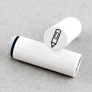 May include: Two white wooden stampers with black ink pads. The stamper on the left has a black ink pad and the stamper on the right has a black ink pad and a black line drawing of a marker on the top.