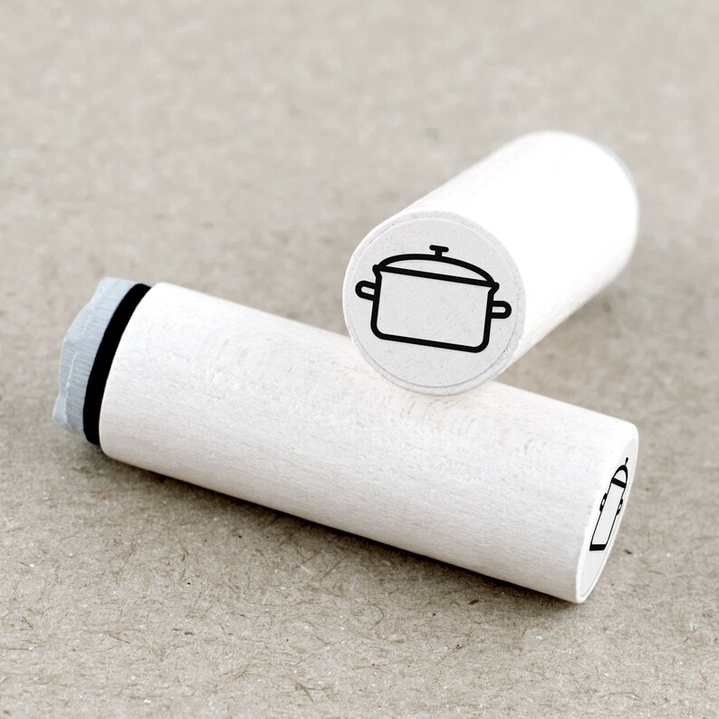DE: Runder Ministempel mit Motiv 'Kochtopf'. Das Stempelgummi ist an ein weiß lackiertes Ahornholz montiert. Das Motiv ist als transparenter Aufkleber auf der Oberseite sichtbar. Der Stempel ist ideal für Bullet Journals, Kalender oder kreative Papiergestaltung.
EN: Round mini rubber stamp with the 'Cooking Pot' design. The rubber stamp is mounted on white lacquered maple wood, with a transparent label on top showing the motif. Perfect for bullet journals, planners or creative paper crafting.