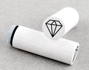 May include: Two white wooden stamps with a diamond design. One stamp is upright, displaying the black diamond graphic. The other stamp is lying down, with a partial view of the diamond graphic. The stamps are on a gray surface.