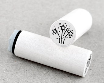 May include: White wooden stamp with a black ink pad and a circular design of fireworks with stars.