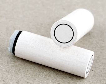 May include: Two white cylindrical stampers with black circles on the top. The stampers are made of wood and have a smooth surface.