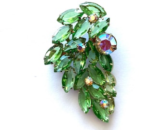 Pode incluir: Um broche vintage com um grupo de pedras de strass verdes iridescentes em um design de folha. O broche tem um acabamento dourado.