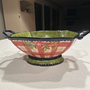 May include: A green and red ceramic bowl with a checkered pattern and floral accents. The bowl has two handles and a pedestal base.