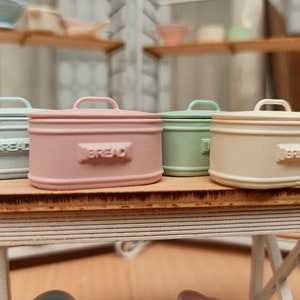 Peut inclure: Quatre boîtes à pain miniatures dans des couleurs pastel, bleu clair, rose, vert et blanc, avec le mot "Pain" en relief sur le devant de chaque boîte.