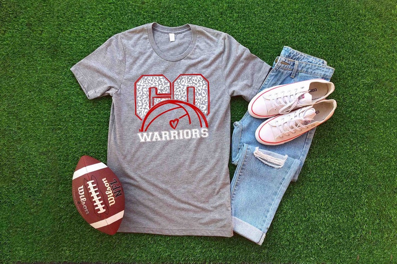 Puede incluir: Camiseta gris con un gr&aacute;fico rojo y blanco de un bal&oacute;n de voleibol con el n&uacute;mero "60" en un dise&ntilde;o de estampado de leopardo y el texto "WARRIORS".