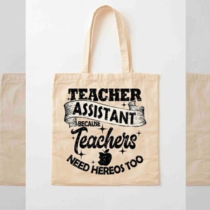 K&ouml;nnte beinhalten: Eine beige Tragetasche mit schwarzem Text, der "Teacher Assistant Because Teachers Need Heros Too" lautet, mit einer schwarzen Apfelgrafik.