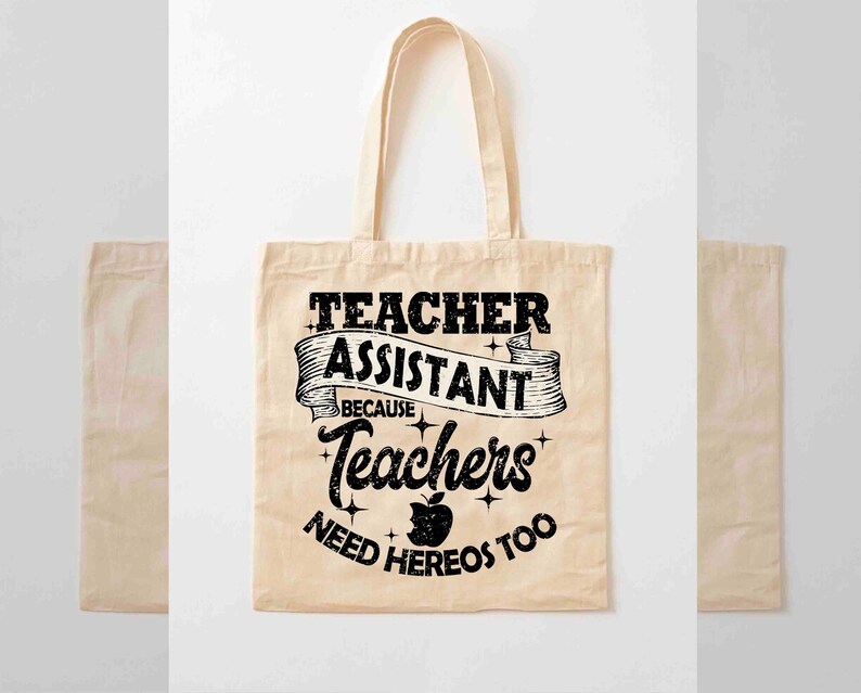 K&ouml;nnte beinhalten: Eine beige Tragetasche mit schwarzem Text, der "Teacher Assistant Because Teachers Need Heros Too" lautet, mit einer schwarzen Apfelgrafik.
