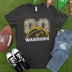 Puede incluir: Una camiseta gris oscuro con un gr&aacute;fico de baloncesto dorado y blanco. El bal&oacute;n de baloncesto tiene un coraz&oacute;n blanco en el centro. El texto "GO WARRIORS" est&aacute; impreso debajo del bal&oacute;n de baloncesto.