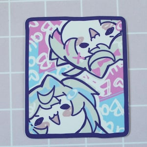 Op de afbeelding: Een rechthoekige sticker met een donkerblauwe rand, met twee stripfiguren met wit en blauw haar. De achtergrond is roze en blauw van patroon. De tekst "kairuis.store" is zichtbaar in de linker benedenhoek.