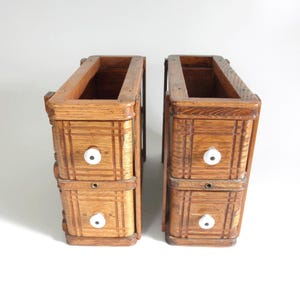 May include: Two antique wooden drawer units with a warm, medium-brown finish. Each unit has two drawers with white knobs and decorative carved details. The open top suggests they may be part of a larger piece of furniture.