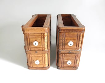 May include: Two antique wooden drawer units with a warm, medium-brown finish. Each unit has two drawers with white knobs and decorative carved details. The open top suggests they may be part of a larger piece of furniture.