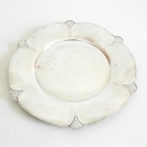 May include: A silver charger plate with a scalloped edge and a raised center. The plate has a slightly worn finish.