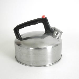 May include: A stainless steel tea kettle with a black handle and a red button on top. The kettle has a rounded body and a spout with a small lid. The handle is arched and attached to the top of the kettle.