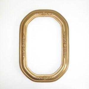 May include: A gold-colored, oval picture frame with ornate floral detailing. The frame has a smooth, glossy finish and a classic, vintage aesthetic. The frame is empty, ready to display a photograph or artwork.