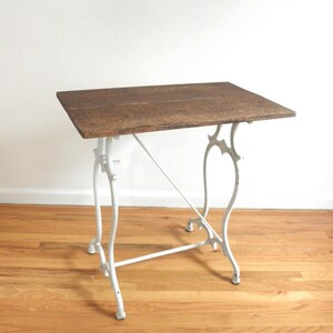 May include: A small, rectangular table with a dark brown wooden top and white, ornate metal legs. The table's legs have a decorative, curved design. The table is approximately 30 inches long and 20 inches wide.