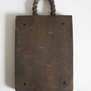 Puede incluir: Un letrero de madera marr&oacute;n oscuro con un asa de cuerda. El letrero tiene cuatro agujeros perforados.