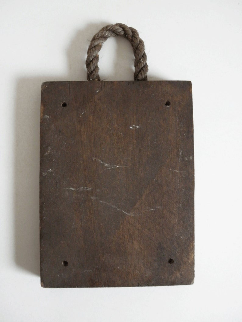 Puede incluir: Un letrero de madera marr&oacute;n oscuro con un asa de cuerda. El letrero tiene cuatro agujeros perforados.