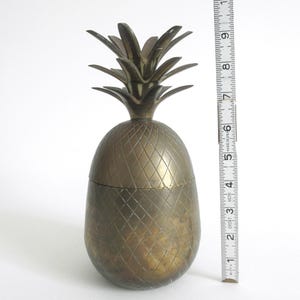 May include: A brass pineapple-shaped container with a textured surface. The container is 6 inches tall.
