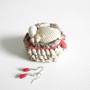 May include: A small seashell box with a red ribbon and a pair of red coral earrings.