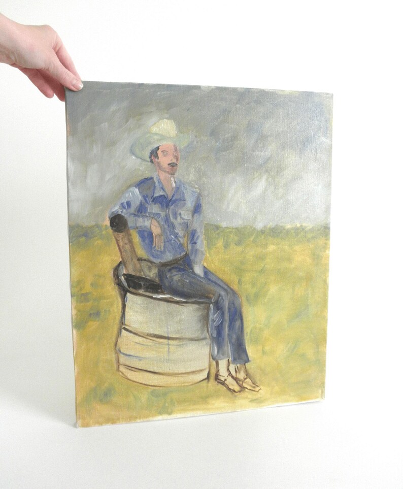 May include: An oil painting on canvas depicting a figure wearing a light-colored cowboy hat and blue clothing, seated on a cylindrical metal drum. The background features a yellow field under a grey, overcast sky, rendered in visible brushstrokes.